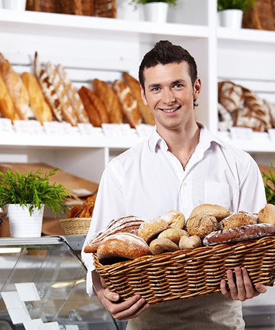 Beneficios del Aval para empresas de Castilla La Mancha - Joven panadero vestido de camisa blanca manga larga cargando cesta de pan dentro de su panadería