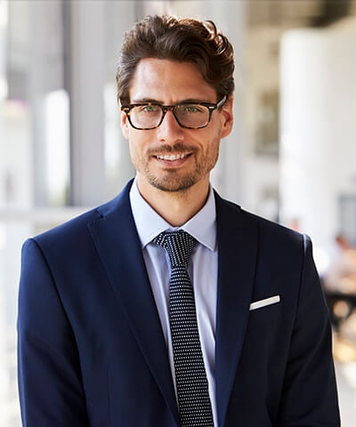 Ventajas de la cartera de inversión gescooperativo - Joven vestido con traje y corbata y gafas sonriendo en su oficina