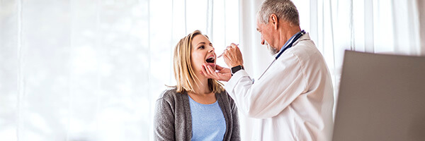 Seguro de Salud - Doctor senior examinando a una joven mujer en su consulta médica Seguro de Salud - Doctor senior examinando a una joven mujer en su consulta médica