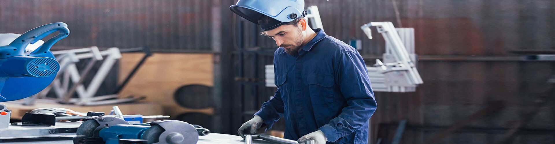 Seguro Multirriesgo Industrial - Hombre con casco y mono azul soldando metal en un taller Seguro Multirriesgo Industrial - Hombre con casco y mono azul soldando metal en un taller