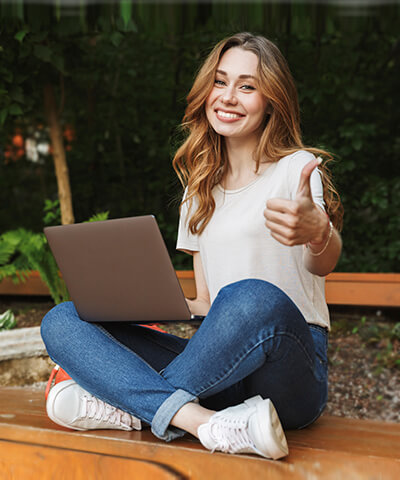 Ventajas para Particulares - Una chica joven sonriendo sentada en el suelo utilizando un portatil Ventajas para particulares - Joven chica sonriendo sentada utilizando un portatil