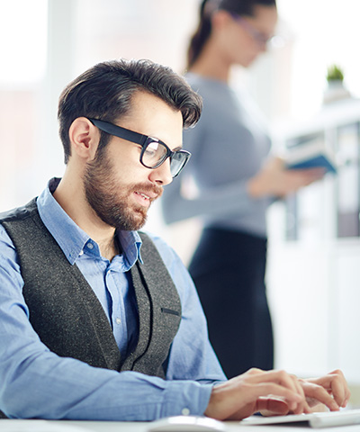 Ejecutivo de gafas negras y barba, vestido de camisa azul, realizando un pago a proveedor en el extranjero a través de Confirming Internacional