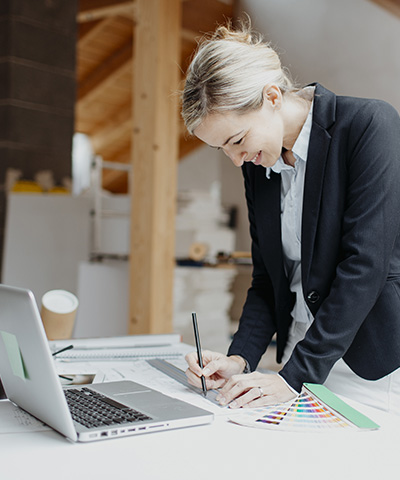 Opciones de financiamiento para empresas Globalcaja   Financiamiento a corto plazo para impulsar proyectos de empresas - Empresaria trabajando en un plano, sujetando un bolígrafo y con un ordenador al frente