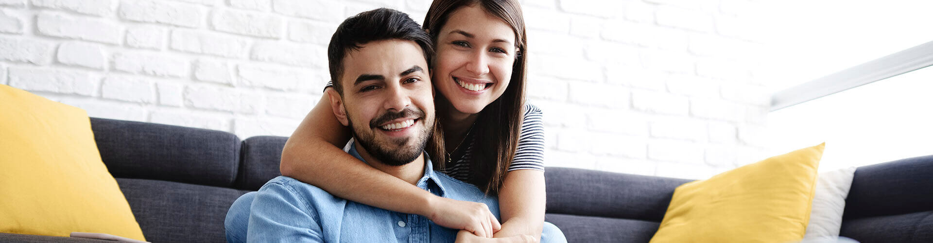 Pareja joven sonriendo en un salón de la casa con un portátil - Seguro de Accidentes Globalcaja