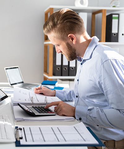 Chico sentado realizando operaciones financieras con calculadora comercial, analizando sus operaciones de cobro de su empresa