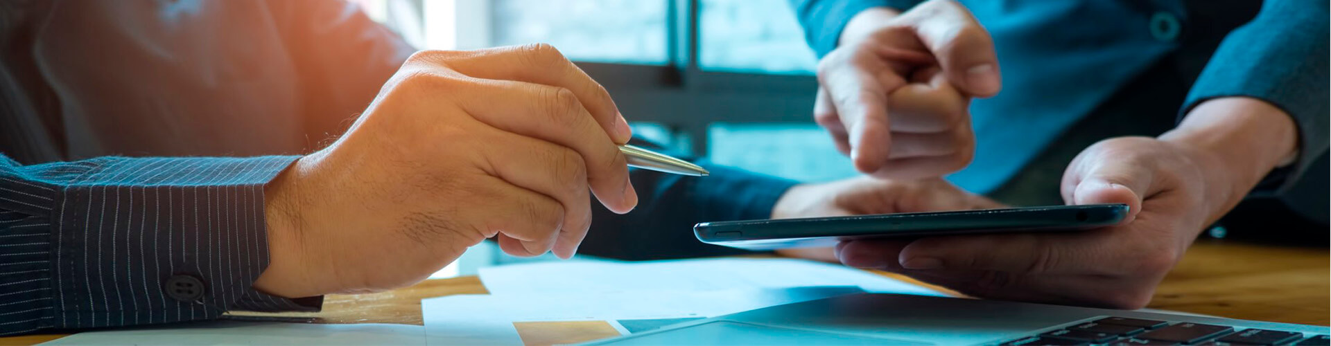 Carteras de Inversión Gescooperativo de Globalcaja Carteras de Inversión Gescooperativo - Dos manos, una con un bolígrafo y otra con una tablet en la oficina, señalando una tablet
