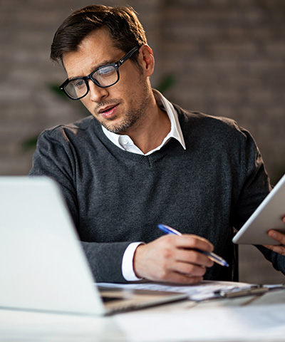 Ventajas de Cuenta Crédito liquidez inmediata para empresas - Hombre empresario con gafas y vestido de suéter gris sujetando boli y tablet, sacando cuentas para mejorar la liquidez de su empresa