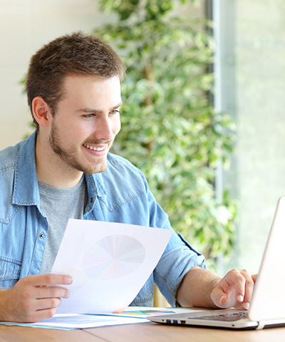 Descuento Comercial, liquidez a través de pagarés, recibos y facturas  -  Chico empresario trabajando en ordenador con una hoja del balance de su empresa