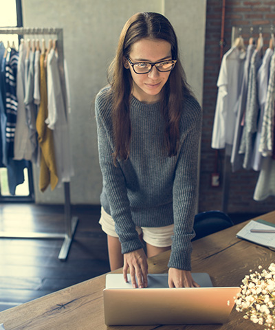 Cobro anticipado a través de Confiming para proveedores - Chica con camisa de rayas trabajando en el mostrador de una tienda con ordenador
