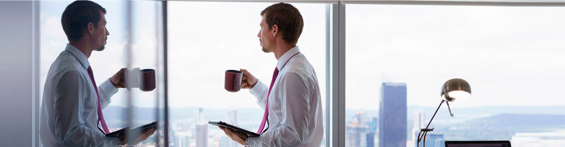 Financiamiento Internacional para empresas con Factoring Financiamiento para empresa factoring Internacional - Un hombre con camisa y corbata, con una taza en la mano mirando por la ventana