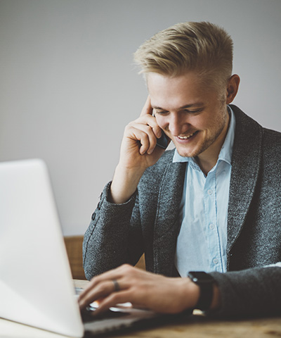 Beneficios de realizar operaciones en divisas con Forward Americano - Chico vestido con chaqueta gris y camisa blanca, conversando por el móvil haciendo operaciones