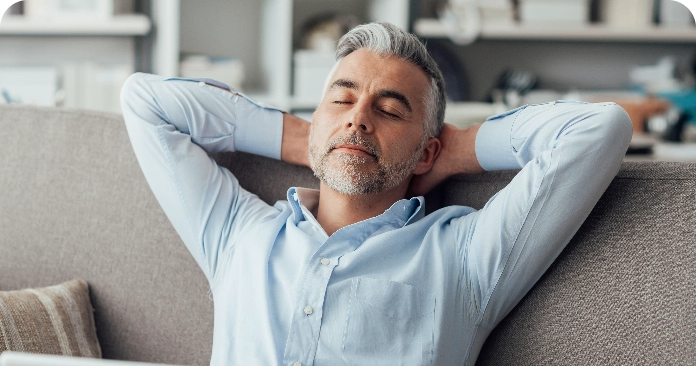 hombre adulto con camisa azul descansa en un sofá de su casa gracias al préstamo personal amigo protegido de Globalcaja