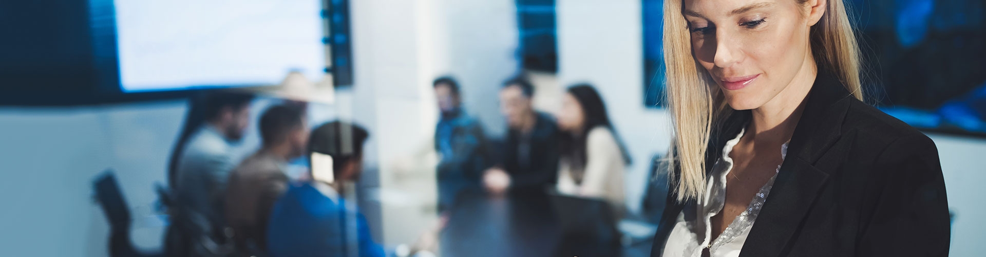 Seguro para empresas Globalcaja - Mujer joven y rubia de negocios con chaqueta de traje negra y camisa blanca utilizando una tablet en una reunión en la oficina