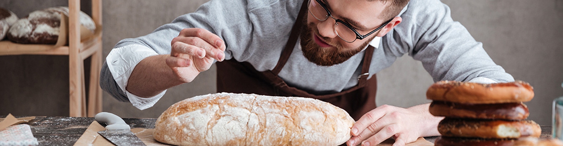 Aval para empresas de Castilla La Mancha - Hombre de barba panadero vestido con delantal marrón y camisa gris, inspeccionando un pan recién hecho