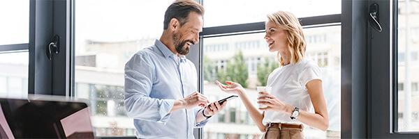 Cartera Premium - Hombre con camisa y movil en la mano, y mujer de negocios con cafe en la mano sonriendo en la oficina Cartera Premium - Hombre con camisa y movil en la mano, y mujer de negocios con cafe en la mano sonriendo en la oficina