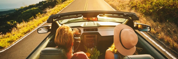Chico y chica en coche paseando por una vía en un día soleado felices porque tienen seguro de automóvil 