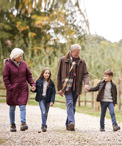 Ventajas para particulares - Abuelos con los nietos sonriendo mientras que caminan por el campo rodeados de árboles