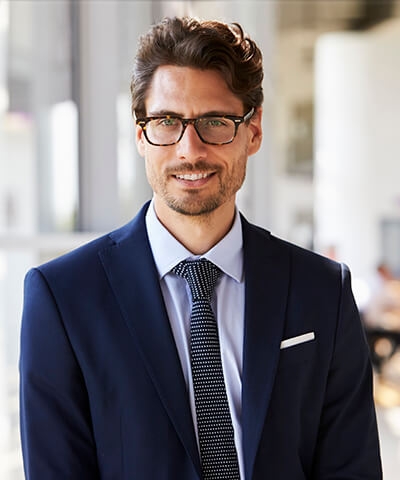 Ventajas para Banca Privada - Joven vestido con traje y corbata y gafas sonriendo en su oficina