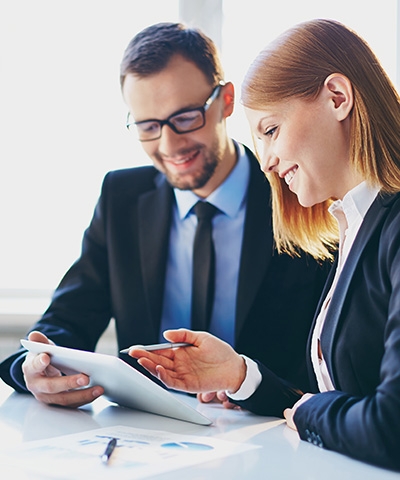 Ejecutiva vestida de traje sonriendo, mostrando en una tablet a empresario, sobre los beneficios de Forfaiting