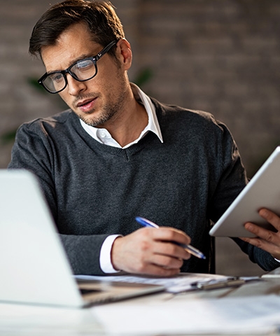 Anticipo de exportaciones para empresas - Chico con gafas y sueter gris trabajando en oficina con el ordenador y una tablet